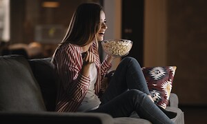 Kvinde ser film på sofaen og nyder hjemmebiografoplevelsen med popcorn