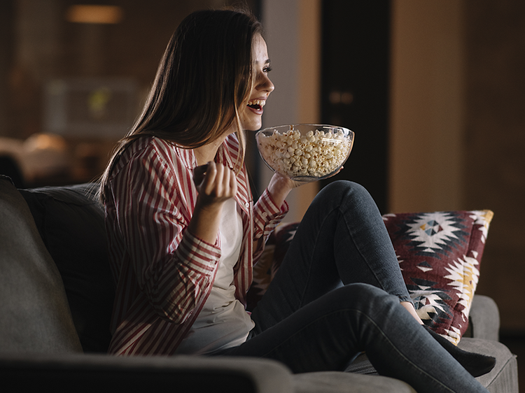 Kvinde ser film på sofaen og nyder hjemmebiografoplevelsen med popcorn