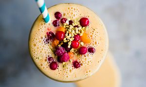 Orange smoothie in a glass with berries on top and a straw