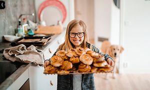 Pige med en bakke med kanelboller i et køkken