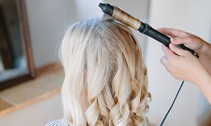 Blond kvinde får håret krøllet med krøllejern