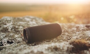 Bærbar Bluetooth-højttaler på en sten med naturen i baggrunden
