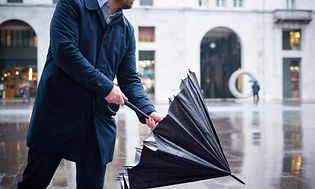 Regnvejrsdag i by, hvor en forretningsmand slår en paraply op