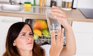 Kvinde ser på kalkbelægning på at drikkeglas fra opvaskemaskinen