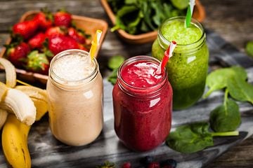 Tre glas med forskellige smoothies omgivet af grøntsager og frugt