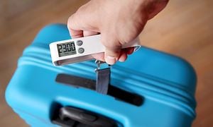 En hånd vejer en blå kuffert med en bagagevægt
