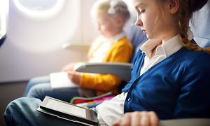 En ung pige sidder i et fly og læser en e-bog ved siden af en lille pige