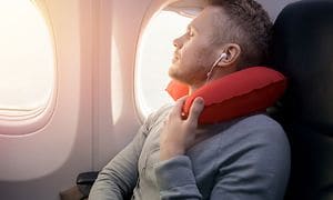 En mand sidder i et fly ved siden af et vindue og sover med en nakkepude