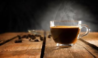 Kop med dampende kaffe på træbord