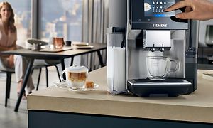 Siemens EQ700 på en køkkenbænk, en kop kaffe og en kvinde i baggrunden