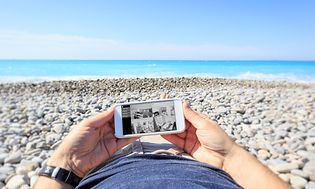 En mand, der ligger på stranden og tjekker overvågningskameraer derhjemme