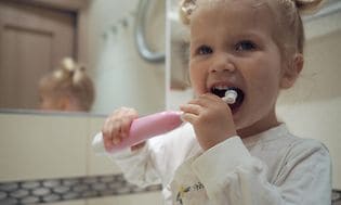 Et glad barn på badeværelset, der børster sine tænder med en elektrisk tandbørste