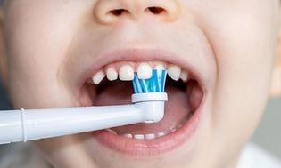Nærbillede af et lille barns mund og et elektrisk tandbørstehoved, der børster tænderne