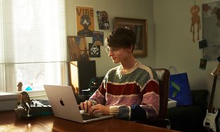 En teenager sidder på sit værelse og arbejder på en MacBook Pro 