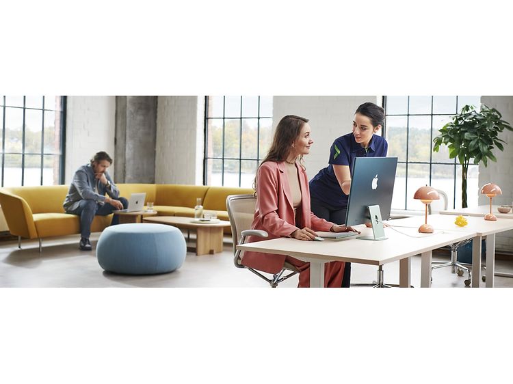 To kvinder ved siden af en iMac, og en mand der arbejder på sin Macbook