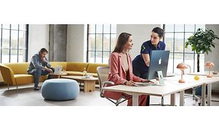 To kvinder ved siden af en iMac, og en mand der arbejder på sin Macbook