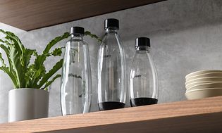 Tre Sodastream-flasker i forskellige størrelser på en hylde