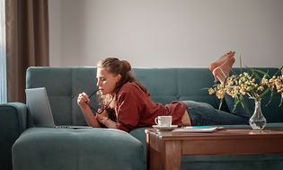 En pige ligger på en sofa og bruger en bærbar computer