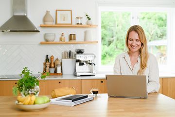 En kvinde sidder i sit køkken og arbejder på sin laptop