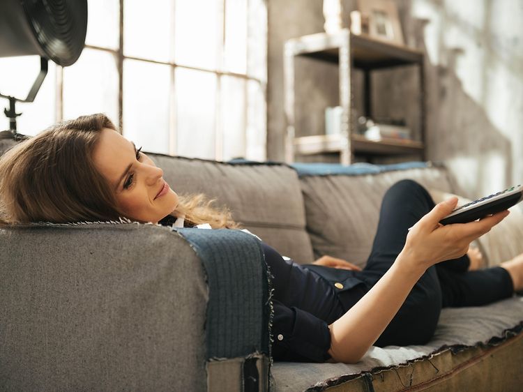 Afslappet kvinde på sofa med fjernbetjening i hånden