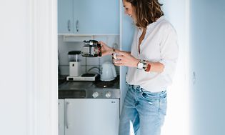 Kvinde, der har skænket en kop kaffe fra en kaffekolbe fra Moccamaster