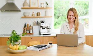 Kvinde, der sidder på hjemmekontor i sit køkken foran sin laptop