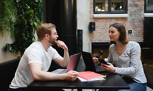 Mand og kvinde taler sammen over hver deres laptop