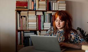 Kvinder arbejder på sin laptop i et rum fyld med bøger