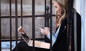 Young woman sitting outside with an iphone and macbook