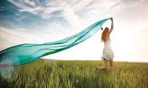 A woman is running in the grass holding a long turquoise scarf