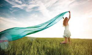 A woman is running in the grass holding a long turquoise scarf