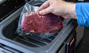 Hånd lægger vakuumforseglet kød i sous vide
