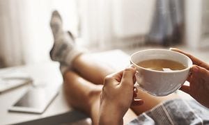 En kop te i hånden på afslappet person i sofa