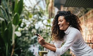 Smilende kvinde på balkong der ser på sin smartphone