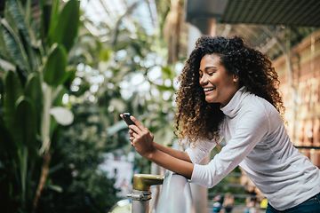 Smilende kvinde på balkong der ser på sin smartphone