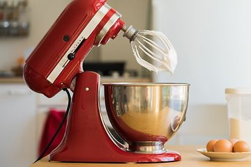 KitchenAid køkkenmaskine på bordet med æg og flormelis ved siden af