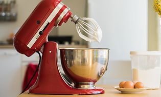 KitchenAid køkkenmaskine på bordet med æg og flormelis ved siden af