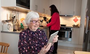 Gammel dame bruger sin tablet i et køkken