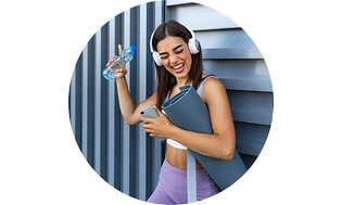 Grinning woman in yoga gear wearing headphones and holding smartphone