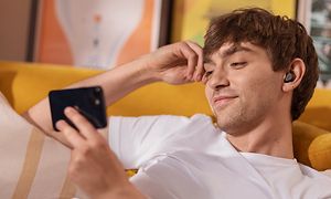 Mand på en sofa med Jabra Elite 5 i ørerne, der holder en smartphone