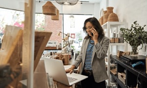 B2B - Elgiganten Control - En kvinde taler i sin smartphone foran sin bærbare computer i en butik desktop