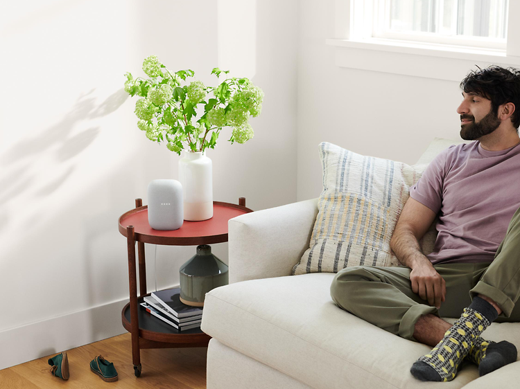 Man sittin in a white sofa while listening to something on his Google Nest Audio
