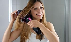 Ung kvinde styler hår med varmluftbørste hjemme