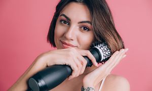 Kvinde på pink baggrund holder styler hår med varmluftbørste