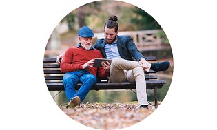 To mænd på en bænk i en park kigger på en tablet