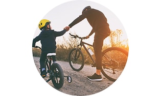 En dreng og en mand holder i hånd mens de cykler i solnedgang