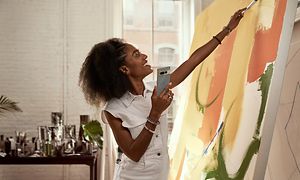 Kvinde står og maler et maleri mens hun holder sin Google Pixel 7 Pro i sin ene hånd