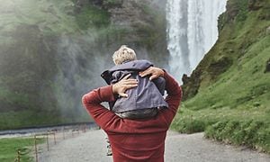 En mand med et barn på skuldrene går tur ved et vandfald