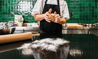 Kok i færd med at ælte dej over et køkkenbord dækket med mel
