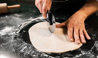 Kok i færd med at skære i pastadej med pastaskærer